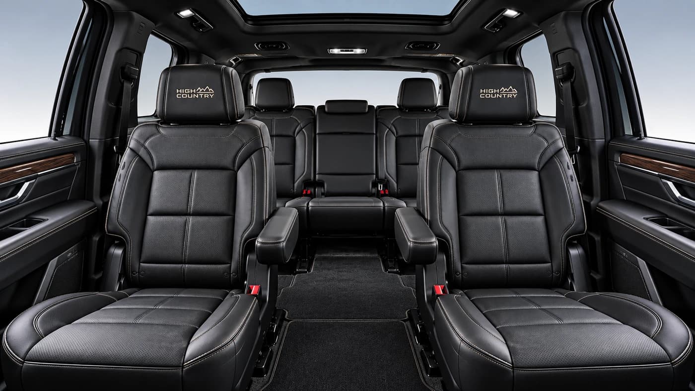 Chevy Suburban interior from the front: black leather seats, wood trim and ambient lighting.