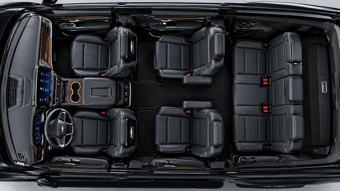 Chevy Suburban interior from above: three rows of black leather seats, dashboard screens and center console.