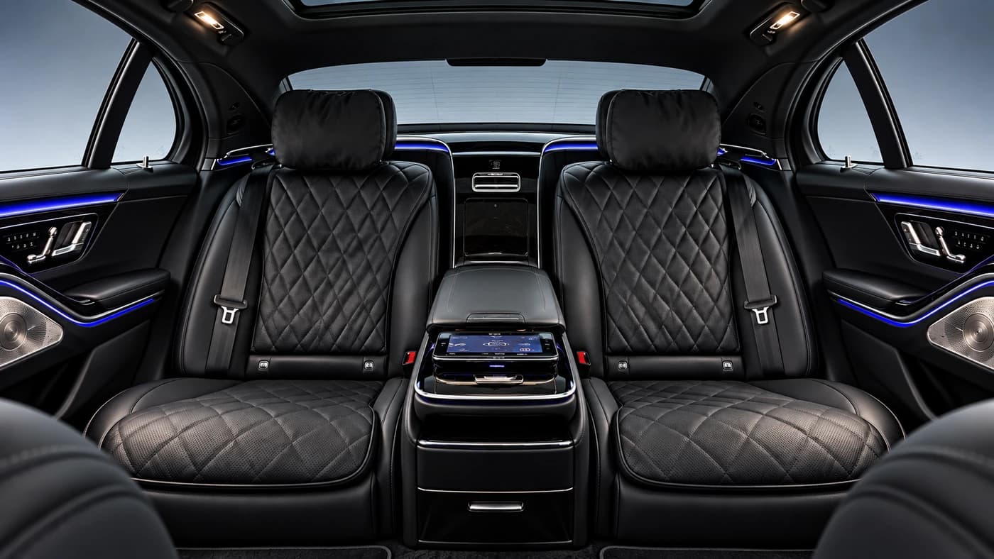 Mercedes-Benz S-Class interior with quilted black leather seats, blue ambient lighting and a center screen.