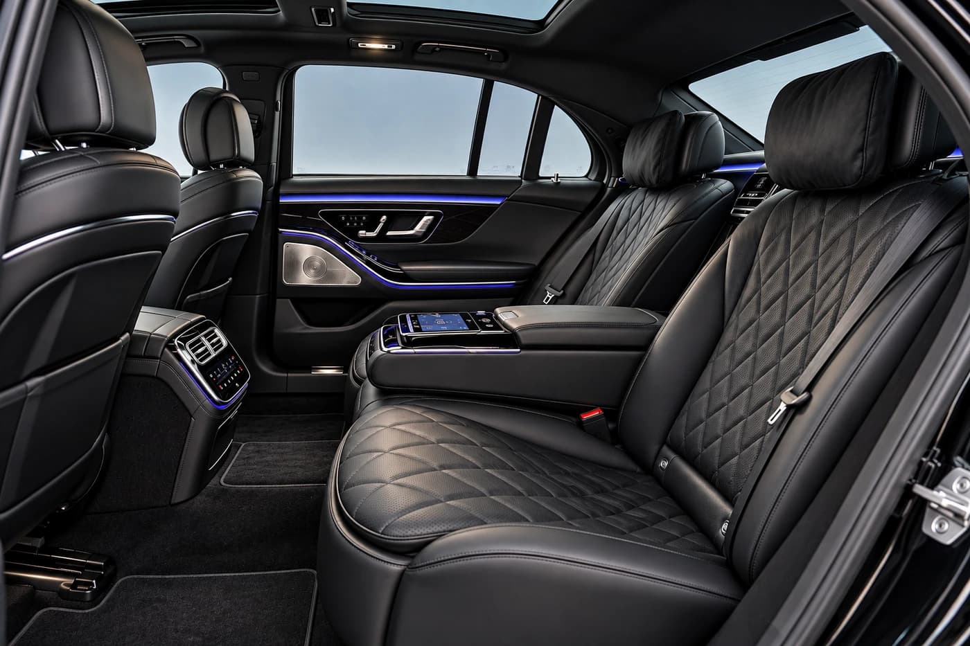 Mercedes-Benz S-Class rear seats in diamond-quilted black leather, with a touchscreen armrest and blue lighting.