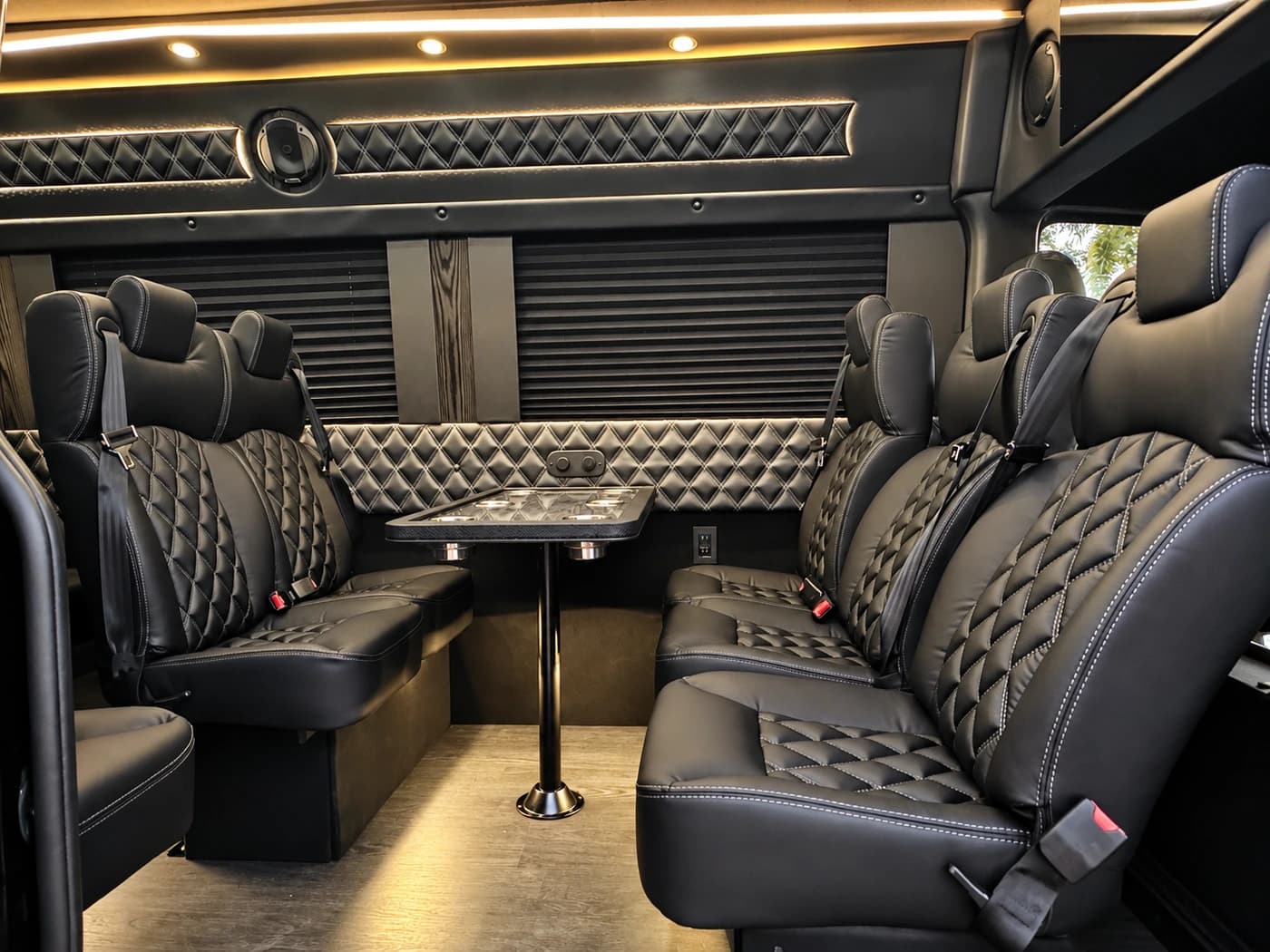 Mercedes-Benz Executive Sprinter cabin with diamond-quilted black leather seats, a central table and ceiling lights.