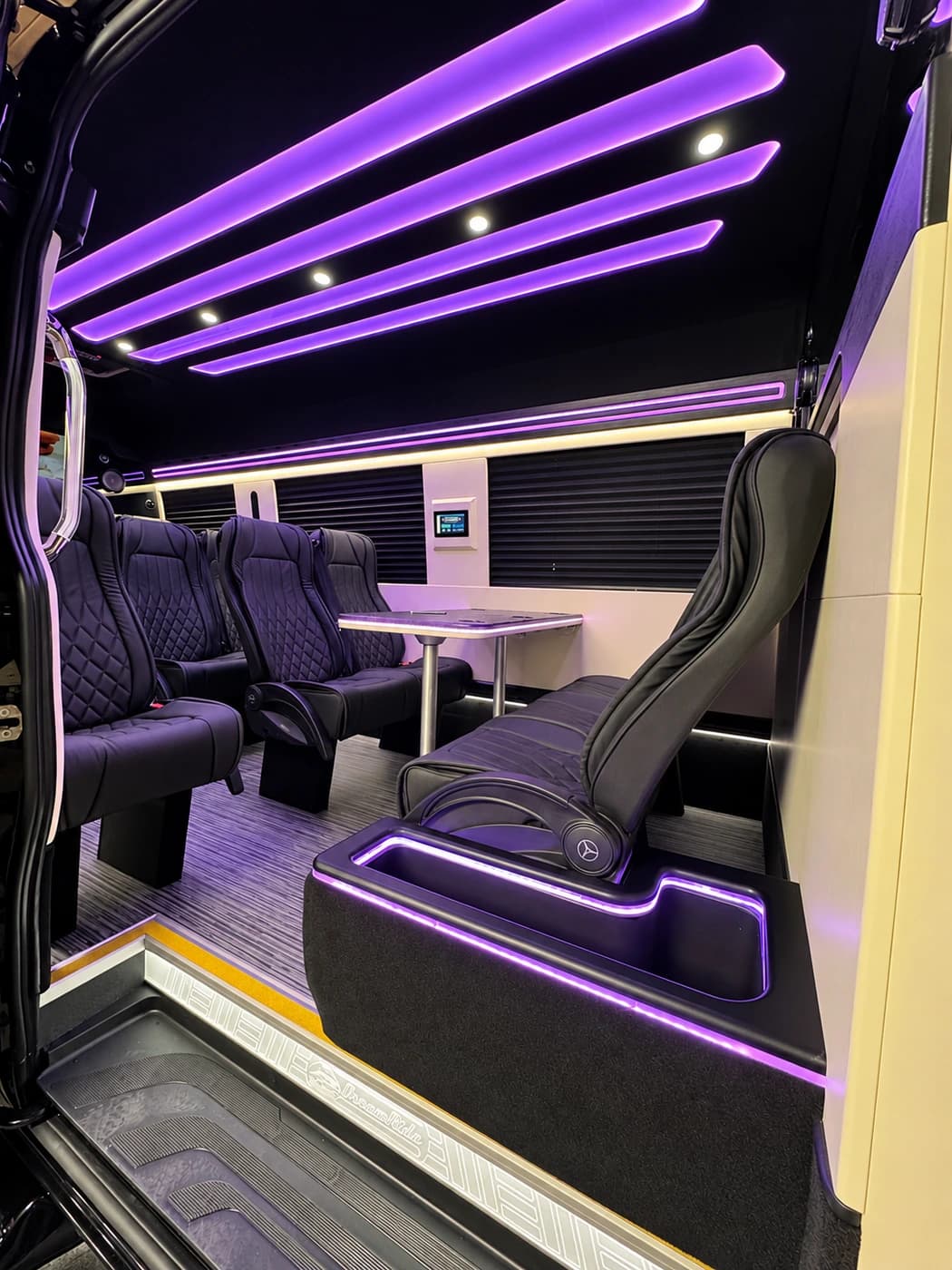 Mercedes-Benz Executive Sprinter cabin with quilted black leather captain's chairs, a table and purple LED lights.