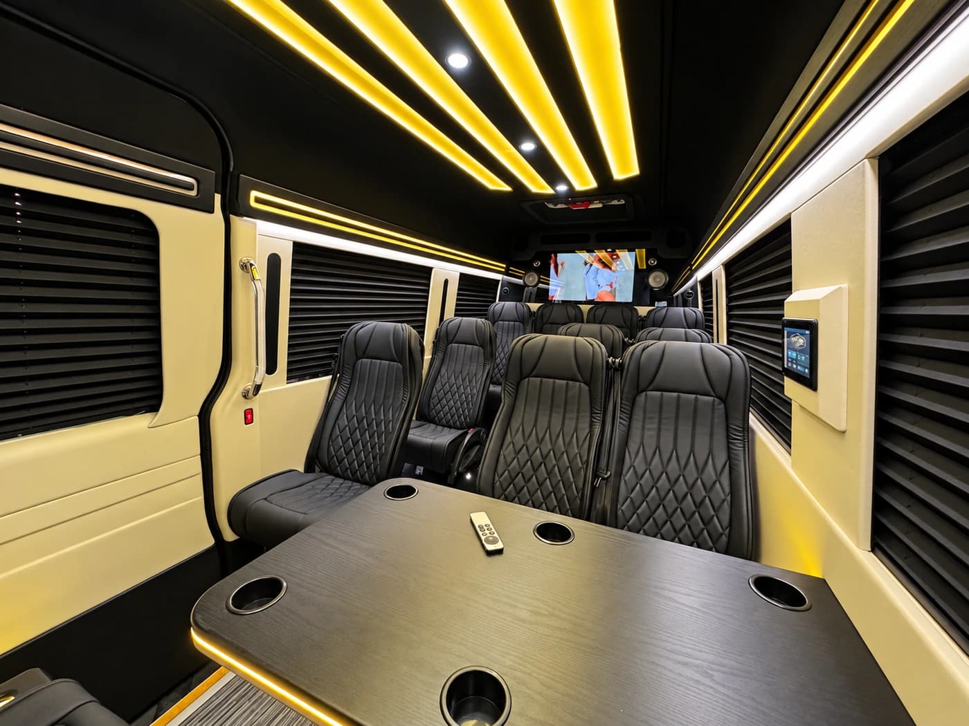 Mercedes-Benz Executive Sprinter cabin with diamond-stitched black leather seats, a table, gold LED lights and a TV.