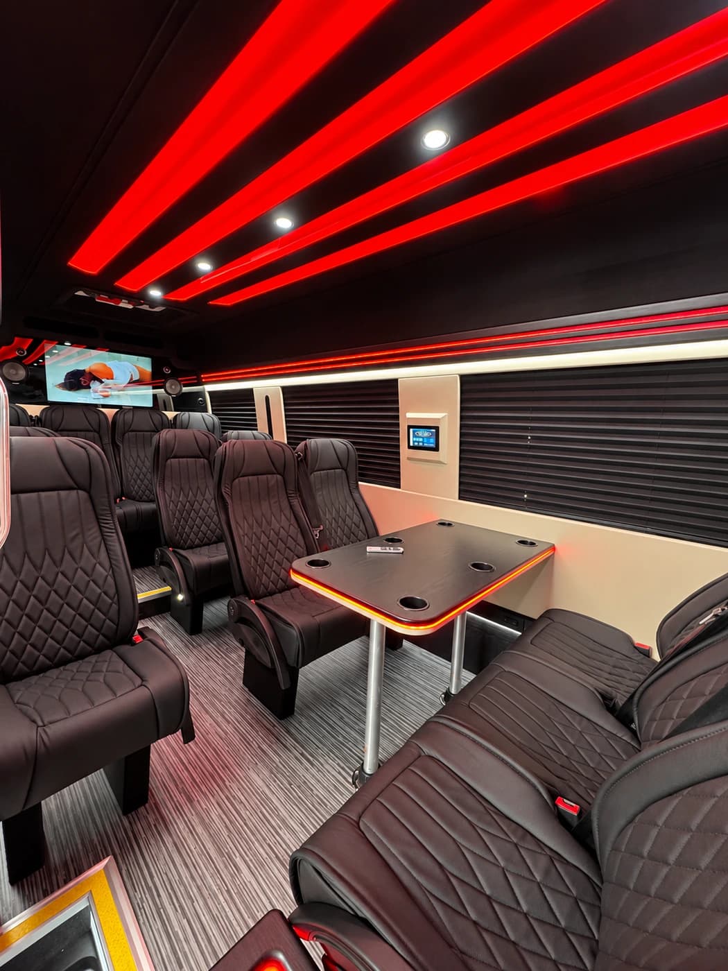 Mercedes-Benz Executive Sprinter cabin with dark leather seats, a central table, red ceiling lights and screens.