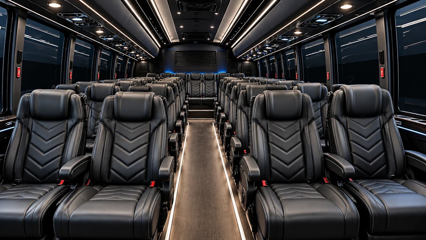 Mini coach interior from the rear: black leather seats with chevron stitching, a central aisle and LED ceiling lights.